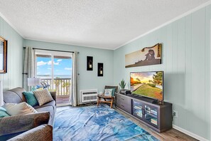 Una sala de estar con un sofá, un televisor, una planta y vistas al exterior.
