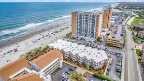A coastal hotel with multiple buildings, a beach, and a parking area.