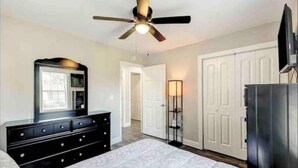 A bedroom with a bed, dresser, TV, wardrobe, and ceiling fan. - Furnished Executive Home - Ideal for Travel Nurses & 30-Day+ Stays (Johns Island)