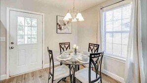 A dining area with a round table set for four, a chandelier, and a window with blinds. - Furnished Executive Home - Ideal for Travel Nurses & 30-Day+ Stays (Johns Island)