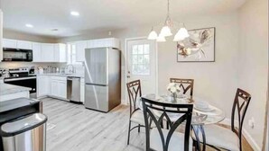 A modern kitchen with white cabinets, a stainless steel refrigerator, and a dining area with a round table and chairs. - Furnished Executive Home - Ideal for Travel Nurses & 30-Day+ Stays (Johns Island)