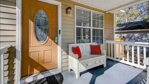 A porch with a wooden door, a white bench with red cushions, and a white railing. - Furnished Executive Home - Ideal for Travel Nurses & 30-Day+ Stays (Johns Island)