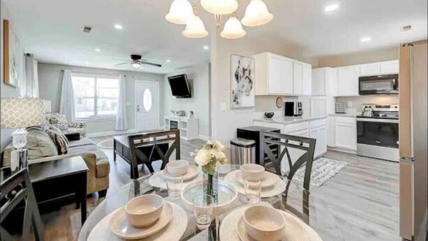 A modern kitchen with white cabinets, a microwave, and a stove. There is a dining area with a table set for four, and a living room with a sofa and a TV. - Furnished Executive Home - Ideal for Travel Nurses & 30-Day+ Stays (Johns Island)