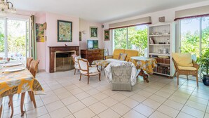 A spacious living room with a fireplace, dining area, and large windows offering a view of greenery.