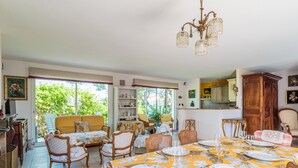 A dining area with a table set for six, surrounded by wicker chairs, a yellow tablecloth, and a chandelier.