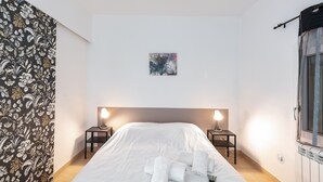 A hotel room with a large bed, two bedside tables with lamps, a painting on the wall, and a window with a curtain.