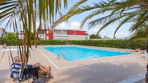 A swimming pool with a clear blue water, surrounded by palm trees and a red building in the background.