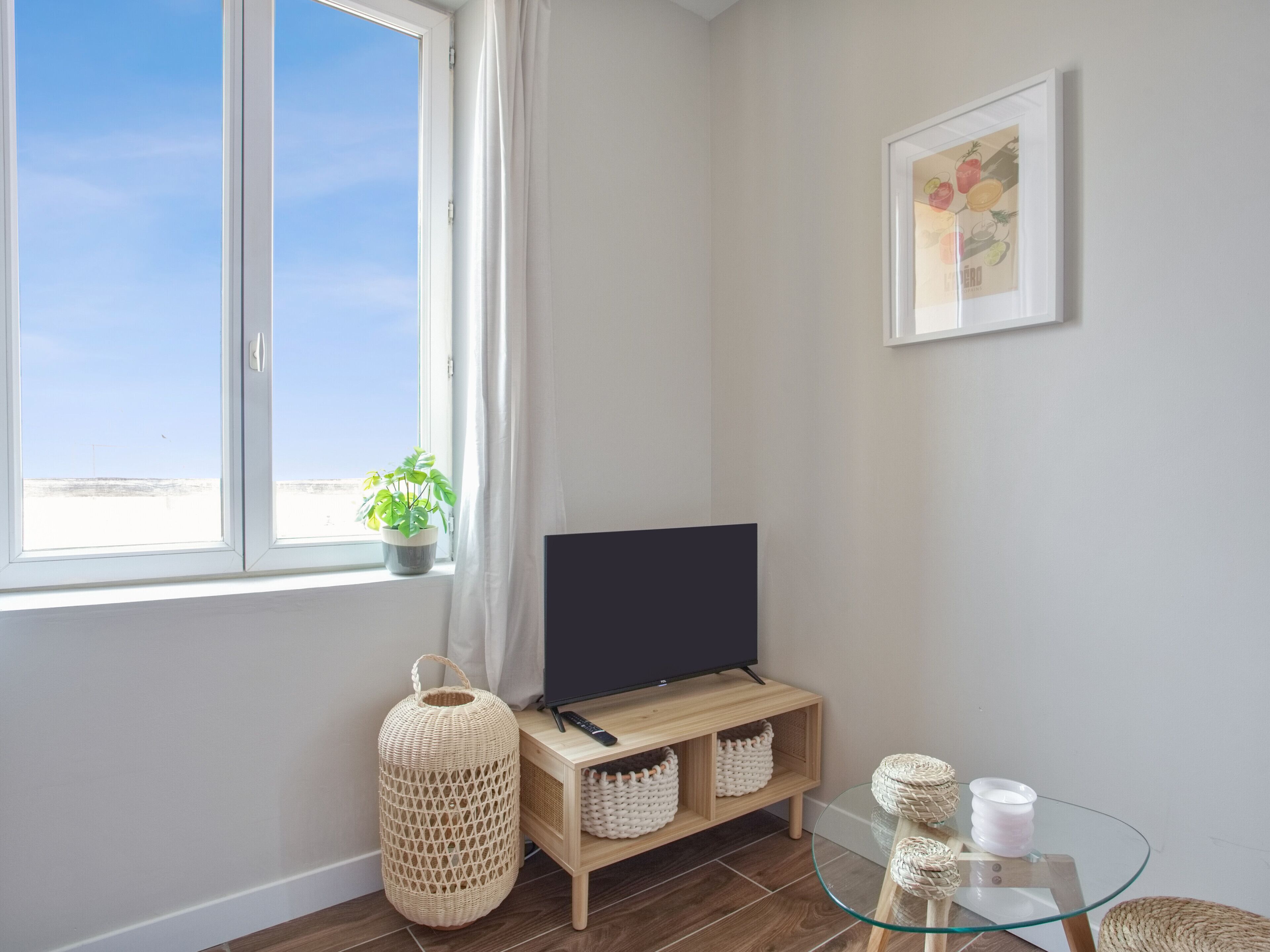 A modern living room with a large window, a flat-screen TV, a wooden TV stand, wicker baskets, and a glass table.