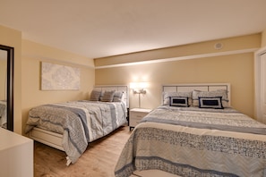 Ein Schlafzimmer mit zwei Betten, jeweils mit gemusterten Bettdecken und Kopfteilen, einem Nachttisch mit Lampe sowie einem an der Wand hängenden Kunstwerk.