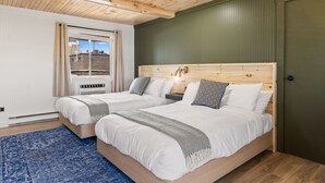 Ein Schlafzimmer mit zwei Betten, Holz-Kopfteilen, einem blauen Teppich und einem Fenster mit Vorhängen.