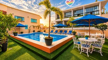 A swimming pool with lounge chairs and umbrellas, surrounded by greenery and a building with large windows.