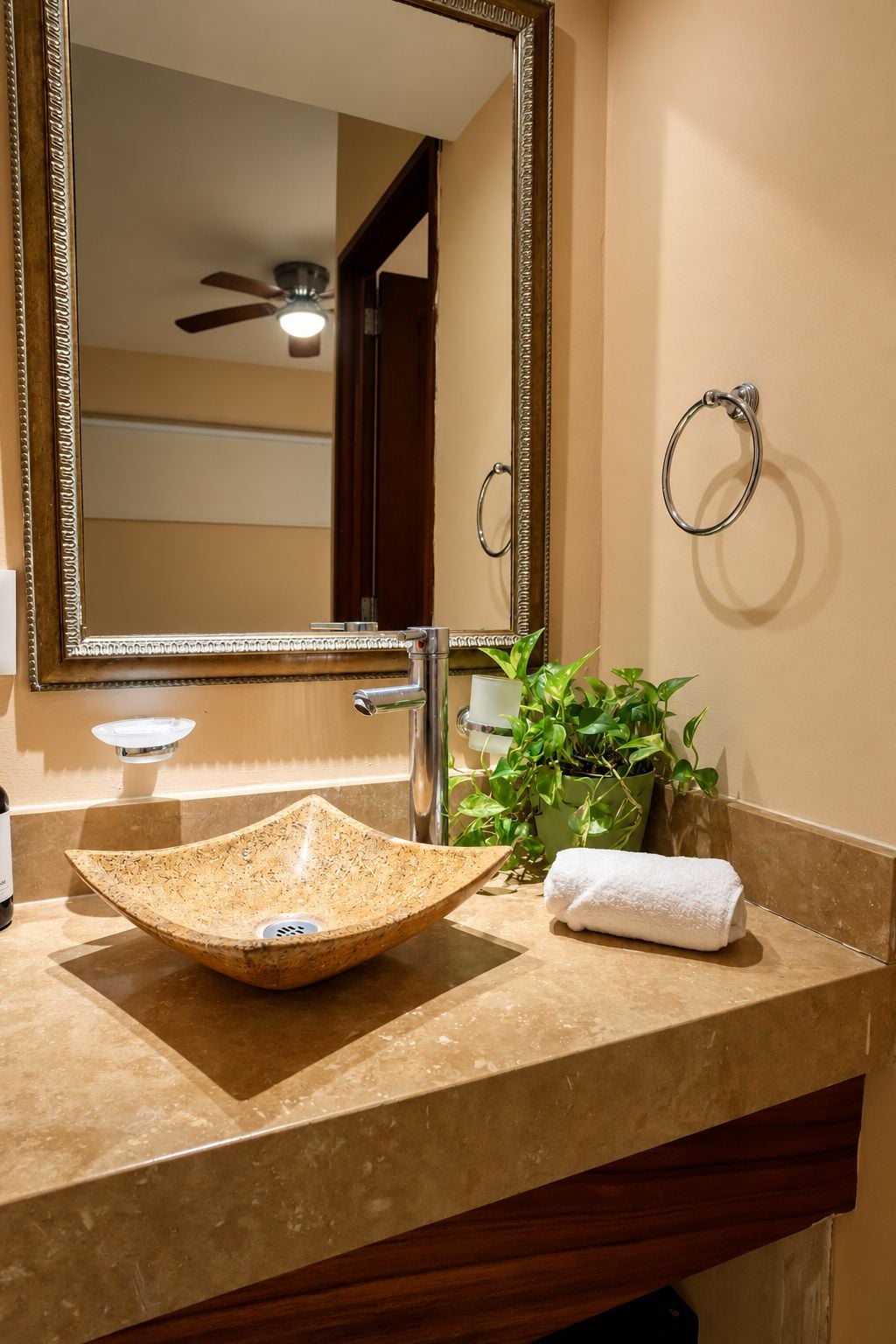 A bathroom with a large mirror, a vessel sink, a towel, and a potted plant.