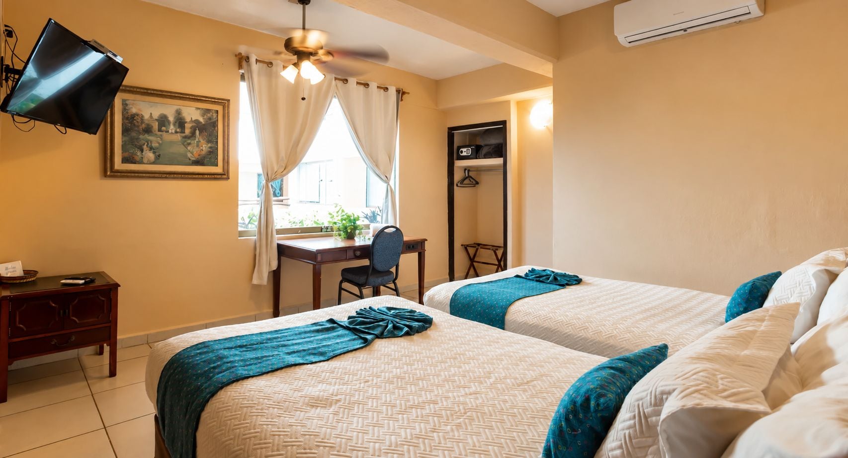A hotel room with two beds, a desk, a chair, a television, and a window with curtains.