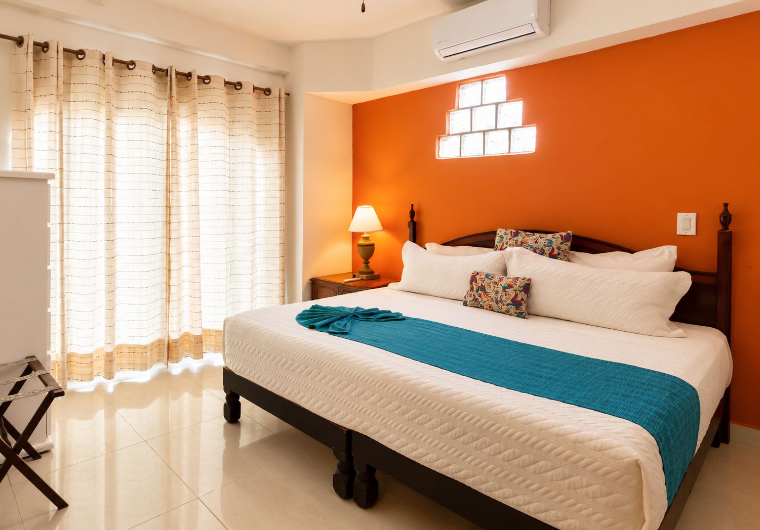 A hotel room with a bed, curtains, a nightstand, a lamp, and an air conditioning unit.