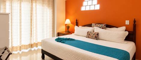 A hotel room with a bed, curtains, a nightstand, a lamp, and an air conditioning unit.