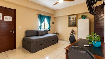 A compact living space with a sofa, a dining table, a ceiling fan, and a refrigerator.