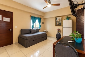 Un espacio habitable compacto con sofá, mesa de comedor, ventilador de techo y refrigerador.