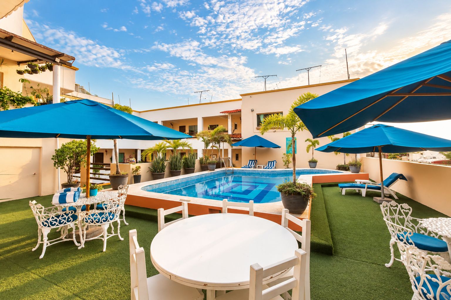 An outdoor swimming pool area with a table and chairs, surrounded by umbrellas and potted plants.