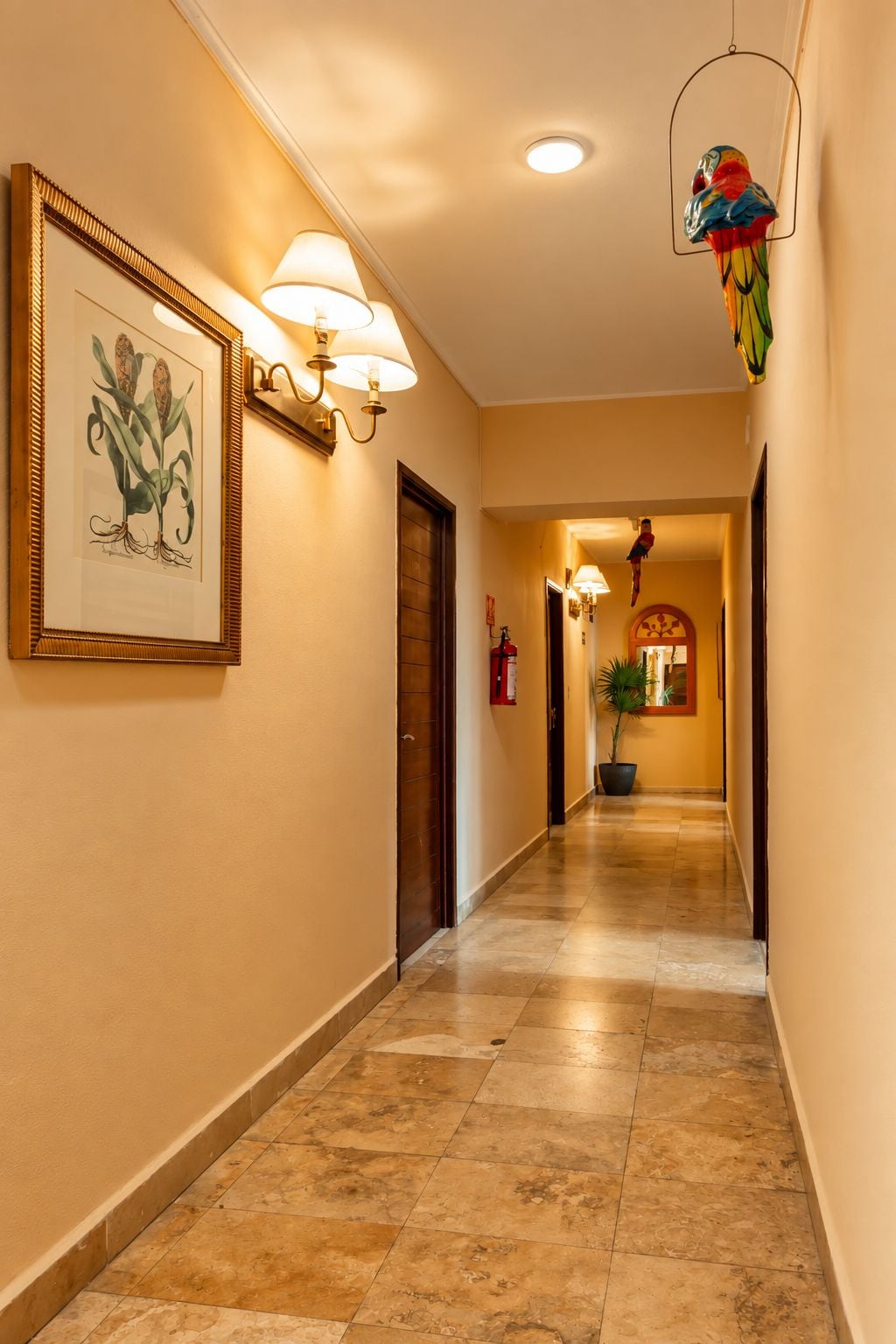A hotel hallway with framed artwork, wall-mounted lamps, and a colorful hanging ornament.