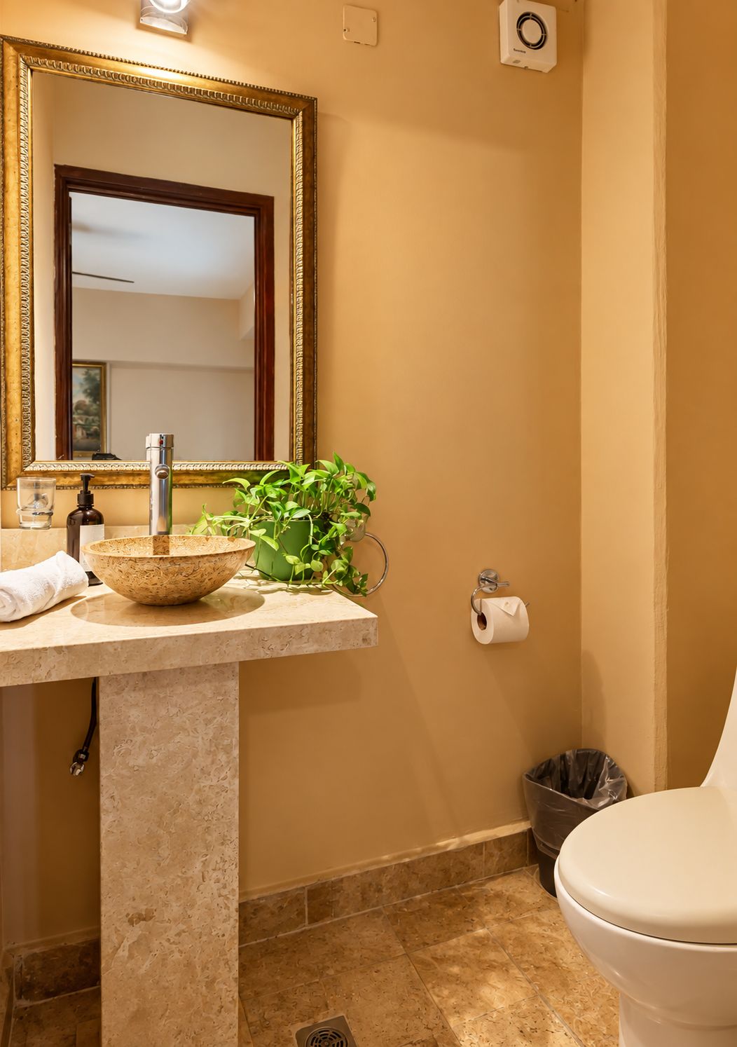 A bathroom with a marble sink, a large mirror, a toilet, and a trash bin.
