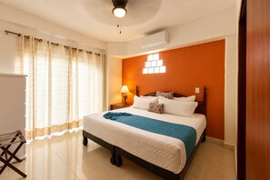Habitación de hotel con cama, cortinas, mesita de noche, lámpara y aire acondicionado.
