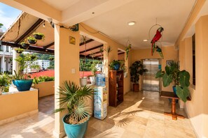 A hotel corridor with potted plants, a bookshelf, and a door leading to a room.