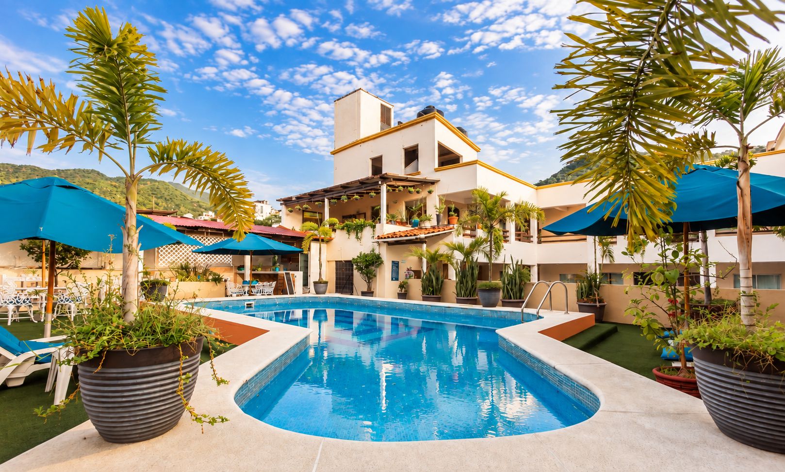 Una piscina con sillones de descanso y sombrillas alrededor, un edificio con techo plano y plantas en macetas.