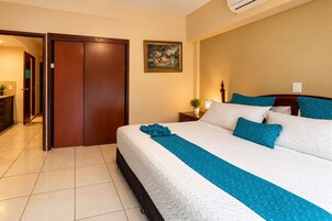 Una habitación de hotel con cama, mesita de noche, un cuadro y una puerta que da a otra habitación.