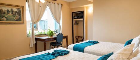A hotel room with two beds, a desk, a chair, a ceiling fan, and a window with curtains.