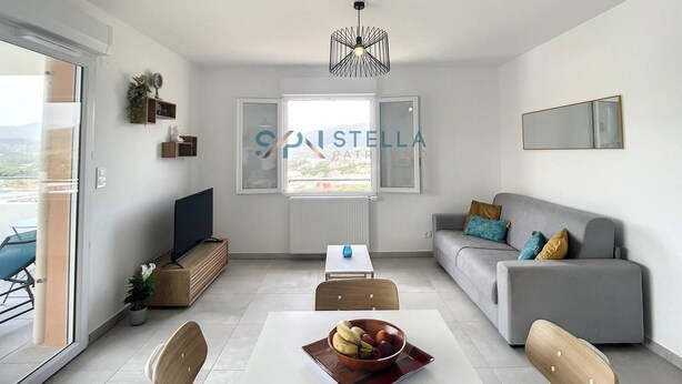 A modern living room with a dining area, a grey sofa, a TV, and a large window. - Superb T2 Splendid view Ajaccio (AJACCIO)