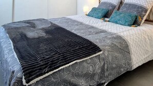 A neatly made bed with a patterned bedspread and pillows, a bedside table with a lamp, and a wall with a decorative panel. - Superb T2 Splendid view Ajaccio (AJACCIO)