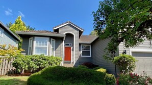 A residential house with a grey exterior, a red door, and a well-maintained front yard with bushes and a lawn. - Ultra-Chic Modern Mid-Century Home in Bethany (Portland)