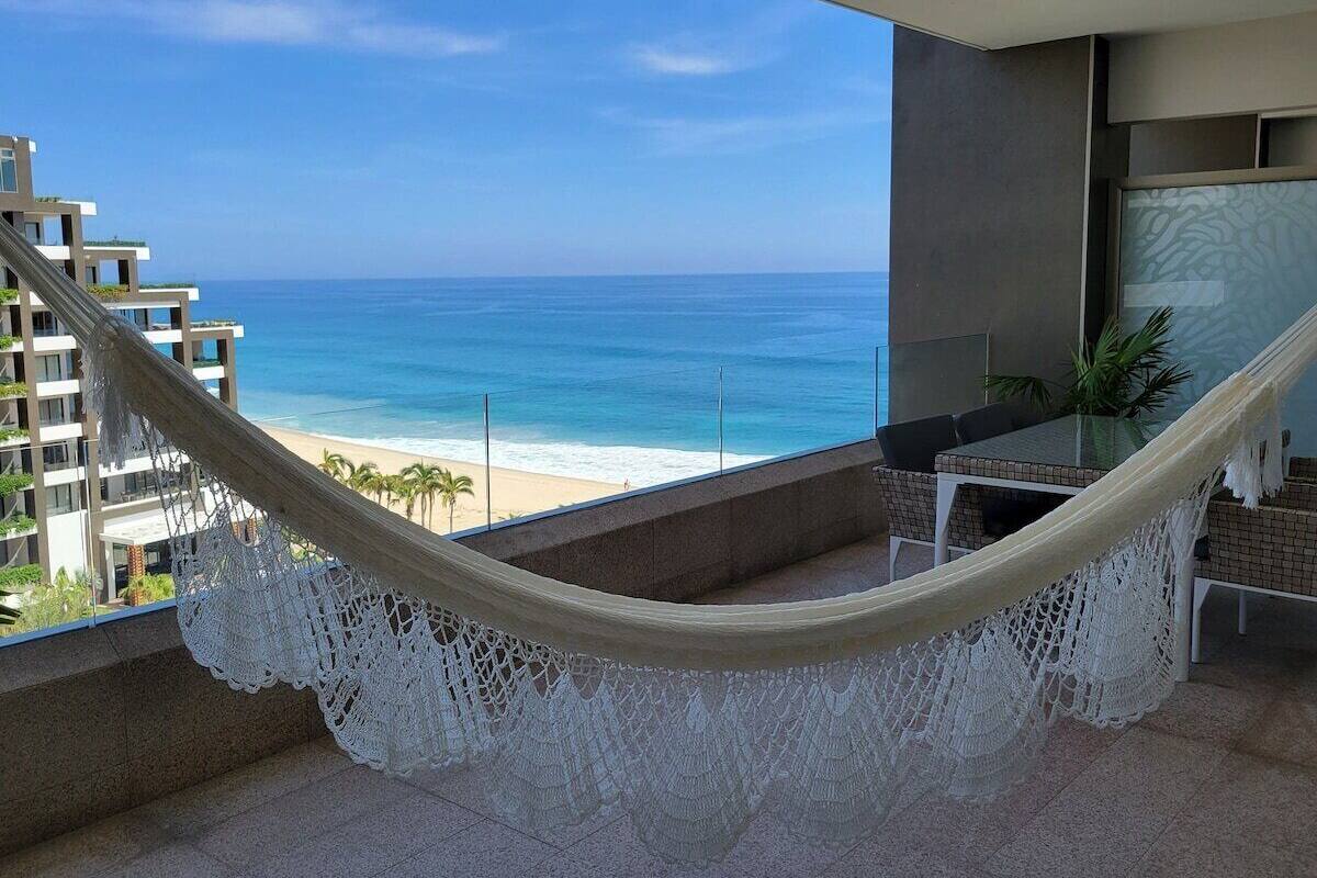 Een hangmat op een balkon met uitzicht op een strand en een helder zicht op de oceaan.