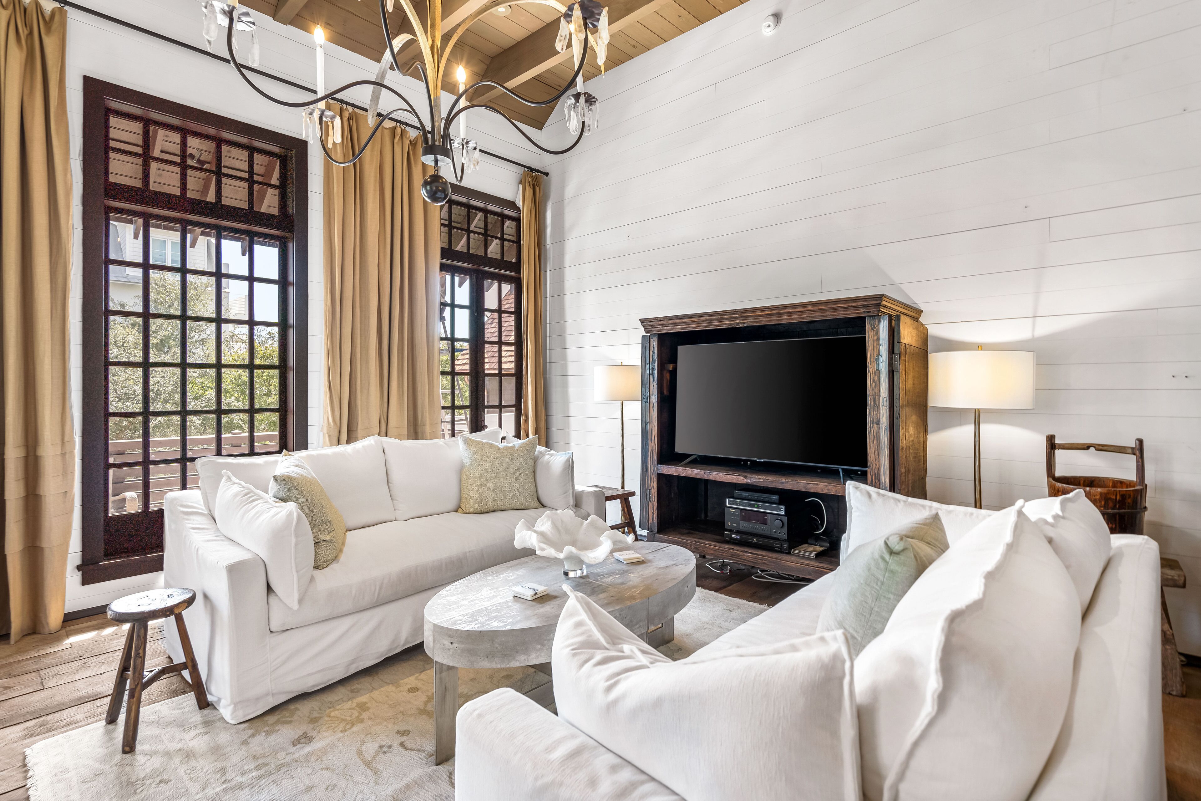 A living room with a white sofa, a coffee table, a TV, and a chandelier.