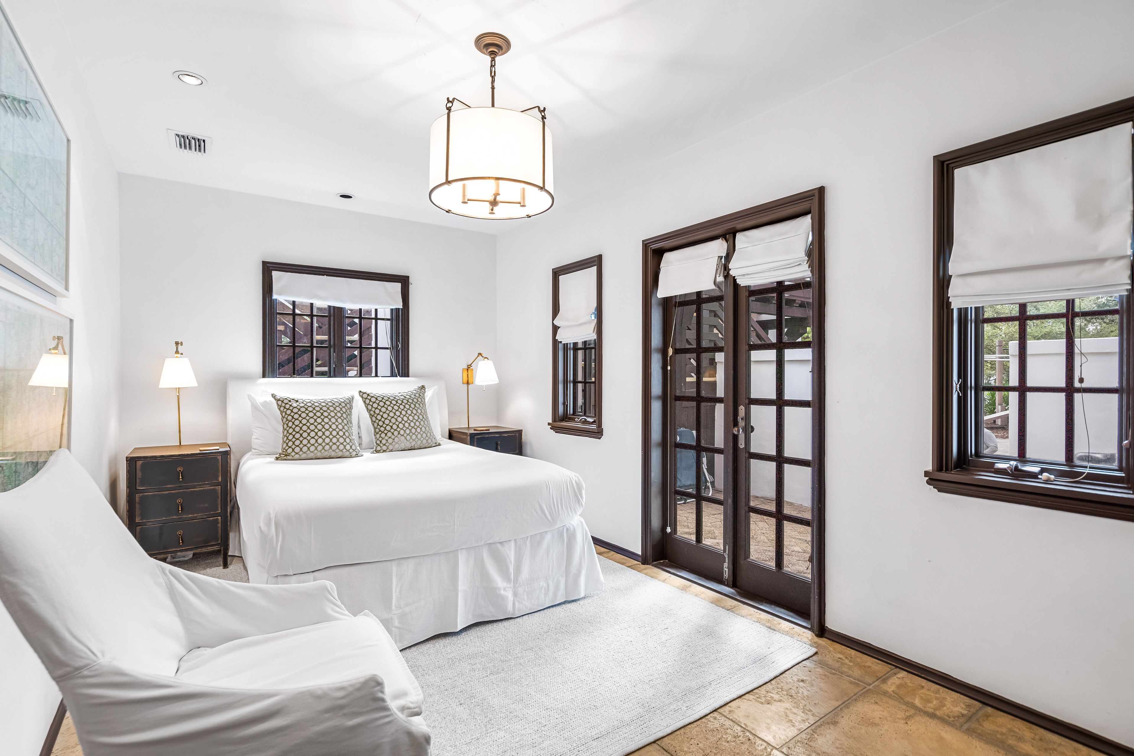 Quarto com cama grande, mesas de cabeceira, uma cadeira e vista através de uma porta de vidro.