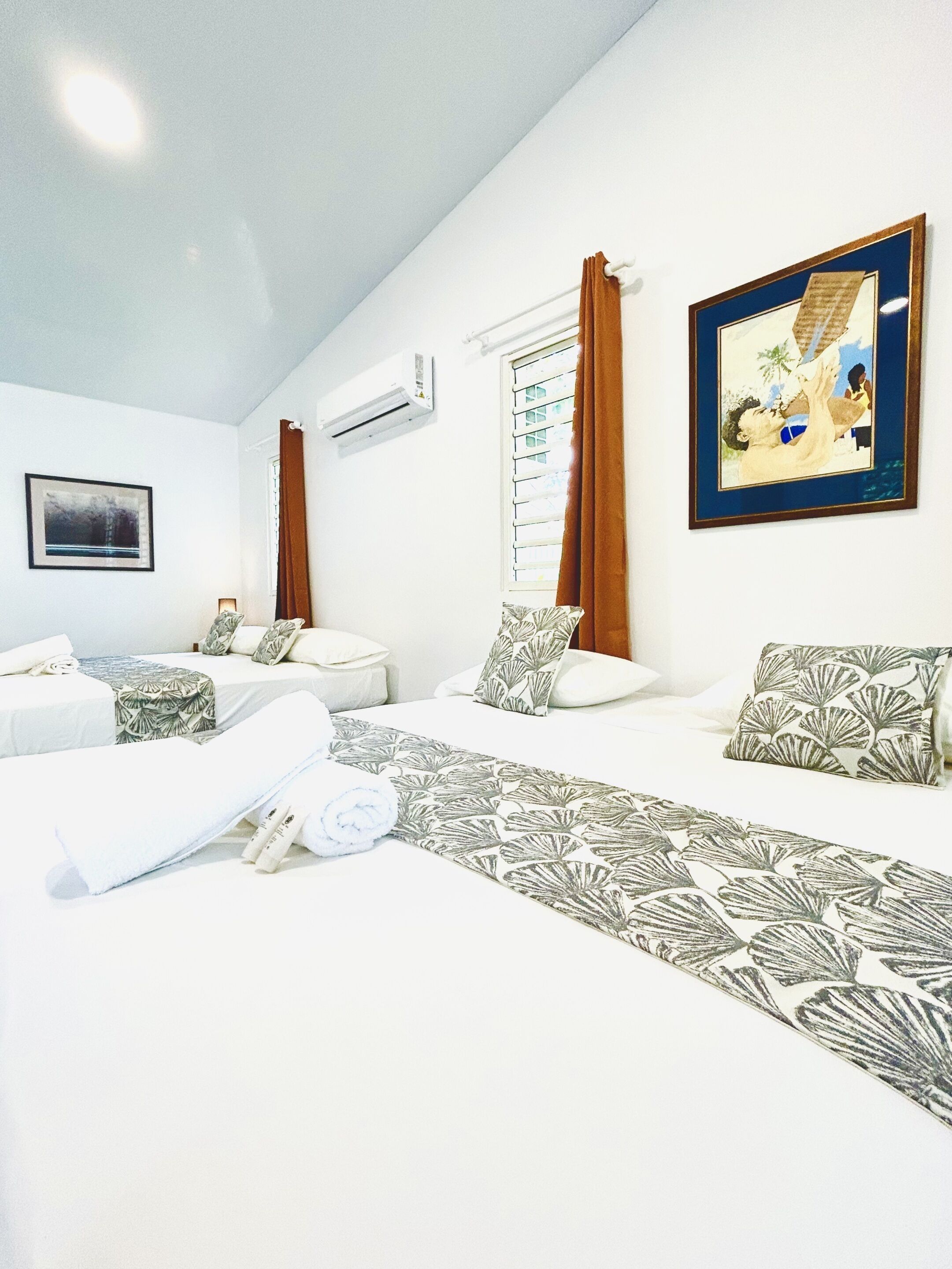 A hotel room with two beds, a large window with curtains, an air conditioning unit, and a framed picture on the wall.