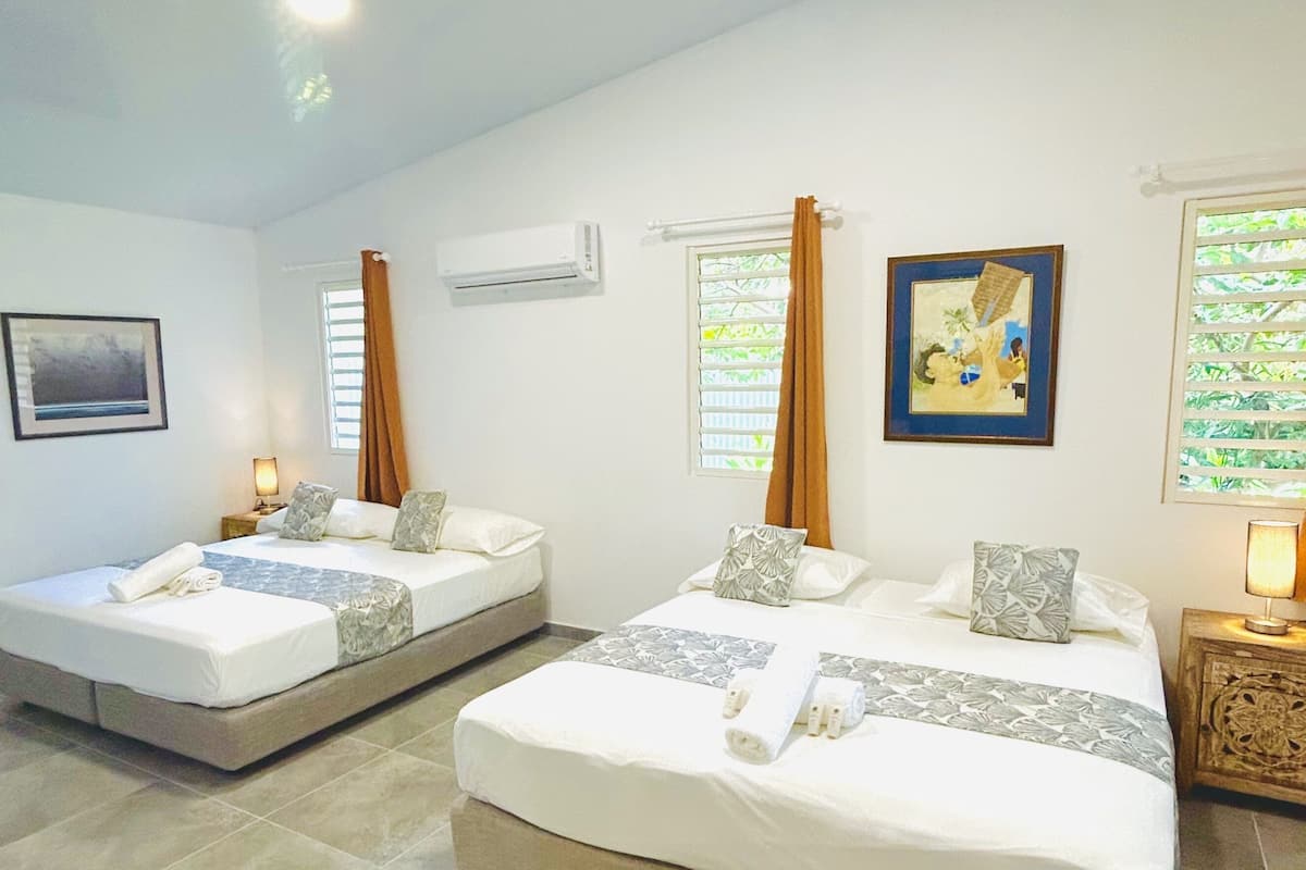 Habitación de hotel con dos camas, una ventana con persianas, un equipo de aire acondicionado y un cuadro en la pared.