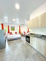 A modern hotel room with two beds, a kitchen area, and a dining table.