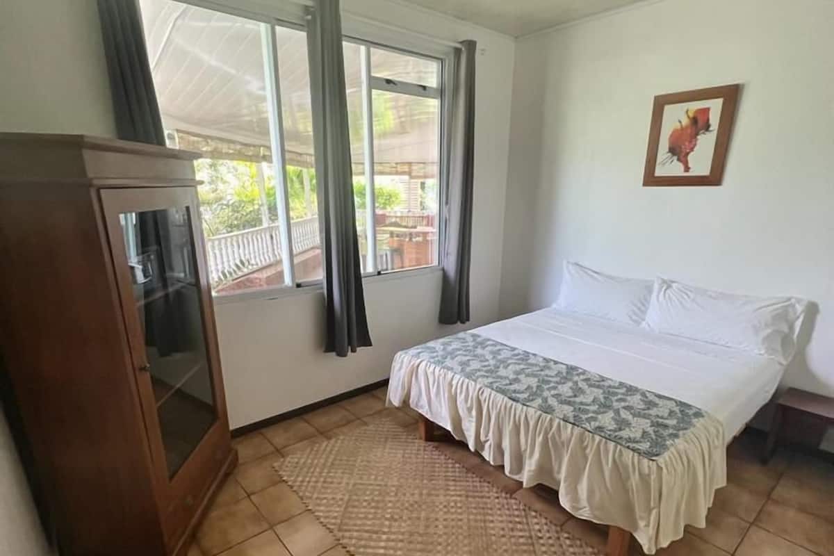 Un dormitorio con cama, un armario de madera, una ventana con cortinas y suelo de baldosas.