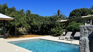 A rectangular swimming pool with clear blue water, surrounded by a light-colored deck. There are lounge chairs and a small waterfall feature on one side.