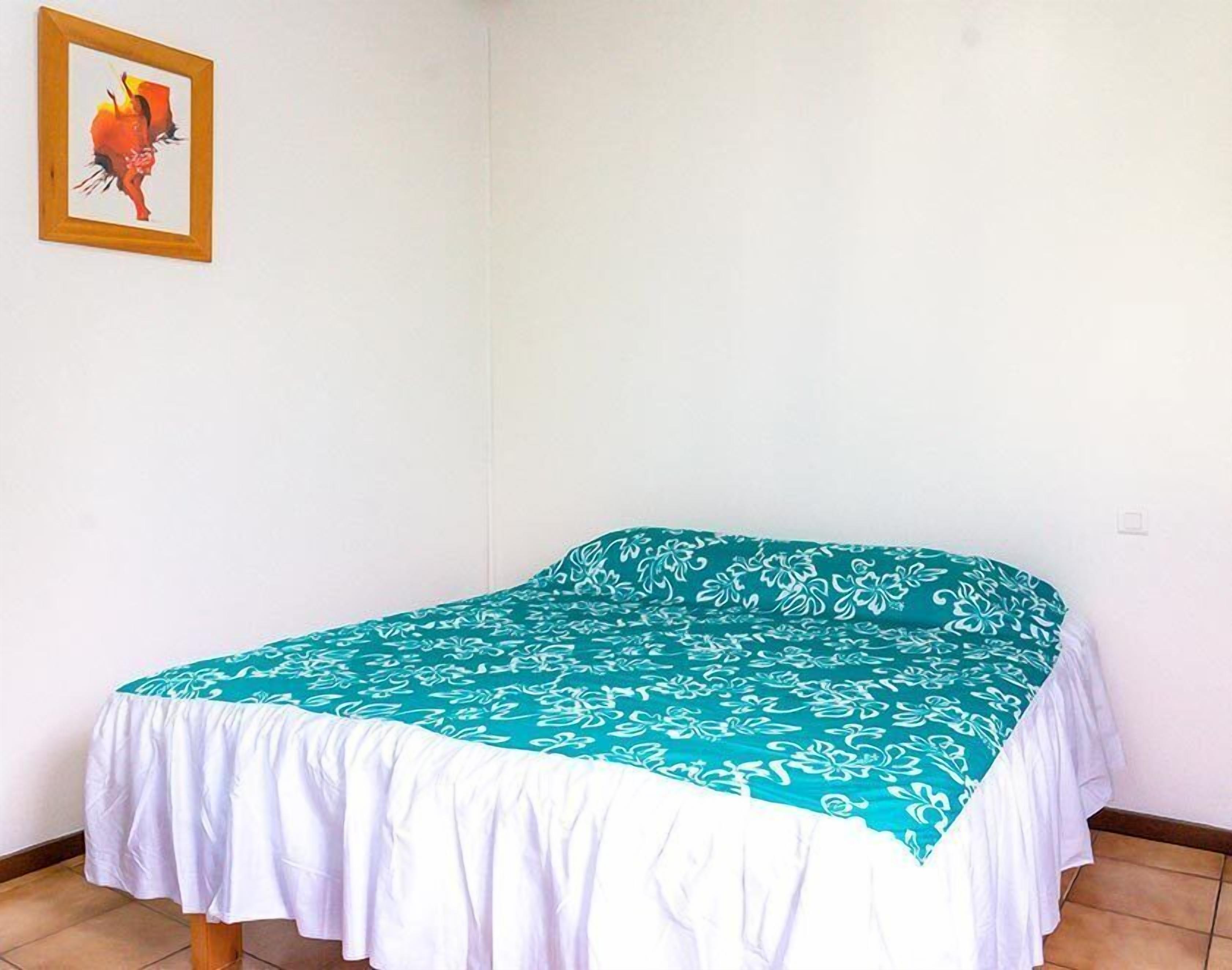 Een eenpersoonsbed met een turquoise en witte spreidek, een wit dekbed met onderlaken en een lijst met een afbeelding aan de muur.