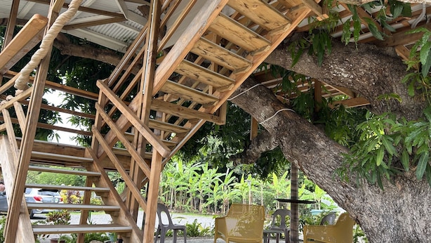 A wooden staircase leading to a covered outdoor area with chairs and tables.