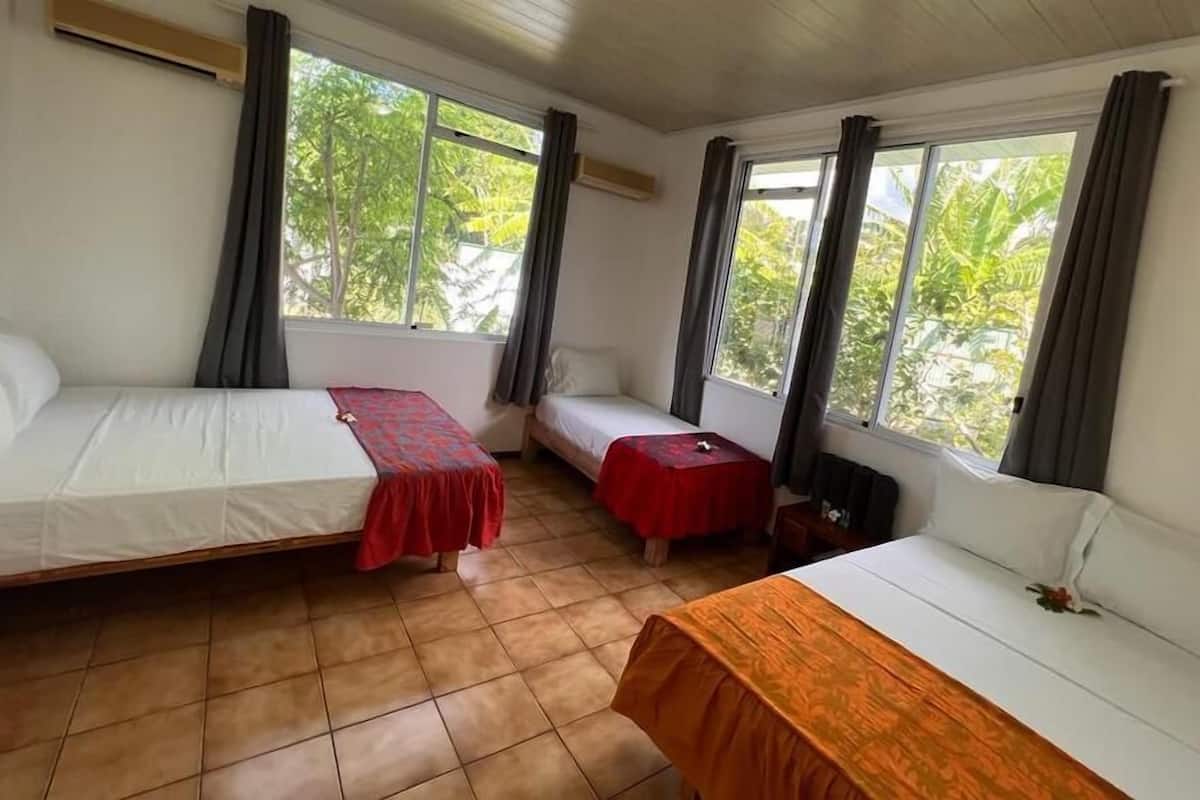 Habitación con dos camas, una mesita pequeña y ventanas amplias con cortinas.