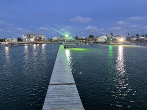 Eine Holzstege, der sich in ruhiges Wasser erstreckt, mit Gebäuden und einem Boot in der Ferne.