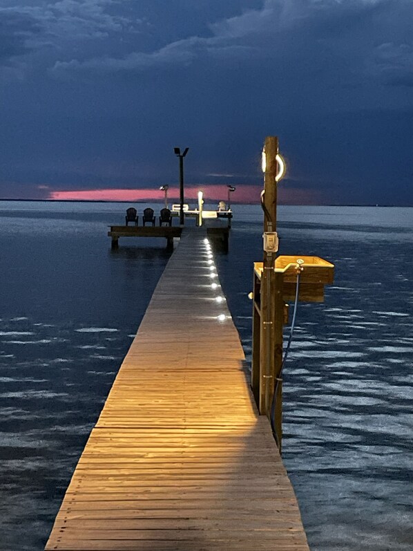 Eine hölzerne Steg, der sich in ruhiges Wasser erstreckt, mit einem Sonnenuntergang im Hintergrund.