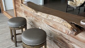 A room with a wooden bar counter, two stools, a television, and a chair with a cushion.