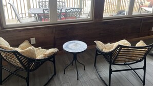 A room with two wicker chairs, a small round table, and a view of outdoor furniture through large windows.