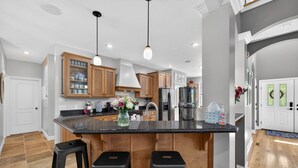 A modern kitchen with wooden cabinets, a granite countertop, and two black barstools. - Amazing Home Near IU's Campus with INDOOR Basketball Gym & Outdoor Pool/Hot tub (Bloomington)