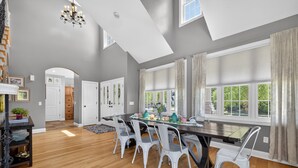 A spacious dining area with a long table, white chairs, and a chandelier. - Amazing Home Near IU's Campus with INDOOR Basketball Gym & Outdoor Pool/Hot tub (Bloomington)