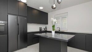 A modern kitchen with dark cabinetry, a central island, and a stainless steel refrigerator. - Amazing home in Zmijavci (Zmijavci)